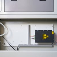 Черный блок высокого напряжения с предупреждающим знаком и клеммными колодками смонтирован на белой панели внутри электротехнического шкафа