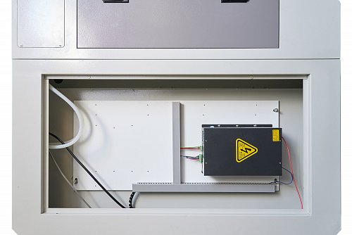 Черный блок высокого напряжения с предупреждающим знаком и клеммными колодками смонтирован на белой панели внутри электротехнического шкафа